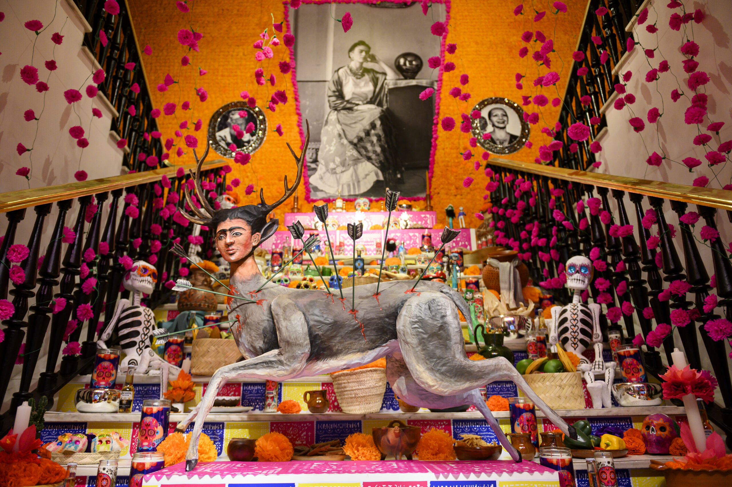 Si piensas que para vivir una auténtica experiencia del Día de Muertos tienes que volar hasta México, ¡te equivocas! La Fundación Casa de México en Madrid vuelve a celebrar este año su séptima edición del Altar de Muertos, y no es cualquier altar. Detrás de su diseño está nada más y nada menos que Eugenio Caballero, el director artístico mexicano galardonado con un Oscar. Así que si te encuentras en Madrid, esta es tu oportunidad para sumergirte en una de las tradiciones más emblemáticas de México sin moverte de la ciudad.  Un viaje entre la vida y la muerte El Altar de Muertos no es simplemente un espacio decorado. Este año, la intervención abarca desde la fachada de la Casa de México hasta su segunda planta, recorriendo escaleras, pasillos y todos los rincones de la casa. El diseño está inspirado en el recorrido simbólico que realizan los difuntos, un trayecto del limbo al mundo de los vivos. Esta idea se refleja en cada detalle del altar, creando una atmósfera única que nos recuerda que la muerte no es el final, sino parte de un ciclo que nos conecta con nuestros seres queridos.  El concepto central del altar es la dualidad: la vida y la muerte, el día y la noche, el sol y la luna, el cielo y el inframundo. Cada espacio está cuidadosamente diseñado para hacerte sentir esta dualidad, desde los colores vibrantes hasta la manera en que las luces juegan con las sombras. Además, por primera vez, la instalación te invita a vivir la experiencia con todos tus sentidos. Es mucho más que un simple altar, es una celebración inmersiva.  El arte detrás del altar La pieza central del altar es un dibujo del maestro Javier Martínez Pedro, quien ha plasmado en su obra un camino que simboliza el viaje de la muerte hacia la vida. Esta ofrenda no solo es una representación visual de la festividad, sino que es un homenaje a una tradición milenaria que sigue viva y que ahora se extiende hasta Madrid.  La elección de Martínez Pedro y de Eugenio Caballero no es casual. Ambos artistas han sabido capturar el alma del Día de los Muertos, combinando elementos prehispánicos con influencias contemporáneas, lo que da como resultado una experiencia artística que va más allá de lo visual. Es una invitación a reflexionar sobre la muerte, pero también sobre la vida, una celebración que nos recuerda que ambos conceptos están profundamente conectados.  ¿Cómo y cuándo visitar el Altar de Muertos? Tienes tiempo hasta el 10 de noviembre para visitar este espectacular altar, así que no hay excusas. Puedes hacerlo de lunes a domingo, y sí, también los festivos como el 12 de octubre, el 1 y el 9 de noviembre. La Casa de México ha organizado recorridos guiados de 25 minutos, en los que podrás conocer todos los detalles del altar y su significado. Si prefieres esta opción, ten en cuenta que es necesario estar suscrito a la newsletter de la fundación para comprar las entradas. Los recorridos guiados son una excelente opción si quieres comprender a fondo la historia y el simbolismo detrás de cada elemento del altar.  Pero si lo tuyo es más pasear a tu ritmo, no te preocupes, también hay horarios de acceso libre. El lunes puedes visitar la casa de 10 a 18:45 horas, mientras que de martes a viernes el acceso es de 10 a 15:30 horas. Y si prefieres aprovechar el fin de semana, el sábado y el domingo está abierto de 10 a 12:30 horas. Así que planifica bien tu visita y no te pierdas esta experiencia única.  ¿Por qué no te puedes perder esta edición? El Día de Muertos es una festividad que ha sido reconocida como Patrimonio Cultural Inmaterial de la Humanidad por la UNESCO, y con razón. Es una celebración que mezcla la solemnidad con la alegría, la memoria con el presente. Este altar no solo es un homenaje a quienes ya no están, sino también un espacio para compartir recuerdos, emociones y, sobre todo, para conectar con una tradición que sigue muy viva.  Madrid ha tenido la suerte de acoger este evento durante siete años consecutivos, y con cada edición, la Casa de México ha sabido superarse. Este año, la apuesta ha sido aún mayor, no solo por el calibre de los artistas implicados, sino por la manera en que han logrado que cada visitante se sienta parte de la tradición.  La posibilidad de experimentar la dualidad entre la vida y la muerte de una forma tan inmersiva es un lujo que no se encuentra todos los días. Así que, si te interesa el arte, la cultura o simplemente quieres conocer una de las tradiciones más hermosas de México, este altar es una parada obligada.  Un evento para todos los sentidos Si algo destaca de esta séptima edición es la capacidad de envolverte por completo en la experiencia. No es solo lo que ves, sino lo que sientes, escuchas y hasta hueles. Cada rincón está pensado para que vivas la festividad de una forma más profunda y personal. La Casa de México se ha convertido en un puente entre culturas, y este Altar de Muertos es un claro ejemplo de cómo las tradiciones pueden viajar, transformarse y, al mismo tiempo, mantenerse fieles a sus raíces.